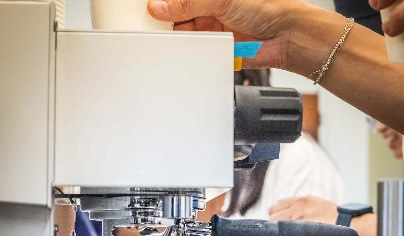 A barista preparing a drink beside an espresso machine in a busy coffee shop